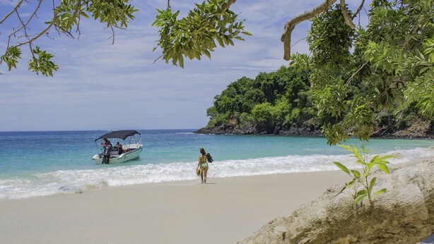 A beach with a boat and a person walking towards the water. - Bocas del Mar Hotel (Boca Chica)