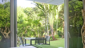 A room with a bed, a table, and chairs, overlooking a lush garden with various trees and plants. - Bocas del Mar Hotel (Boca Chica)