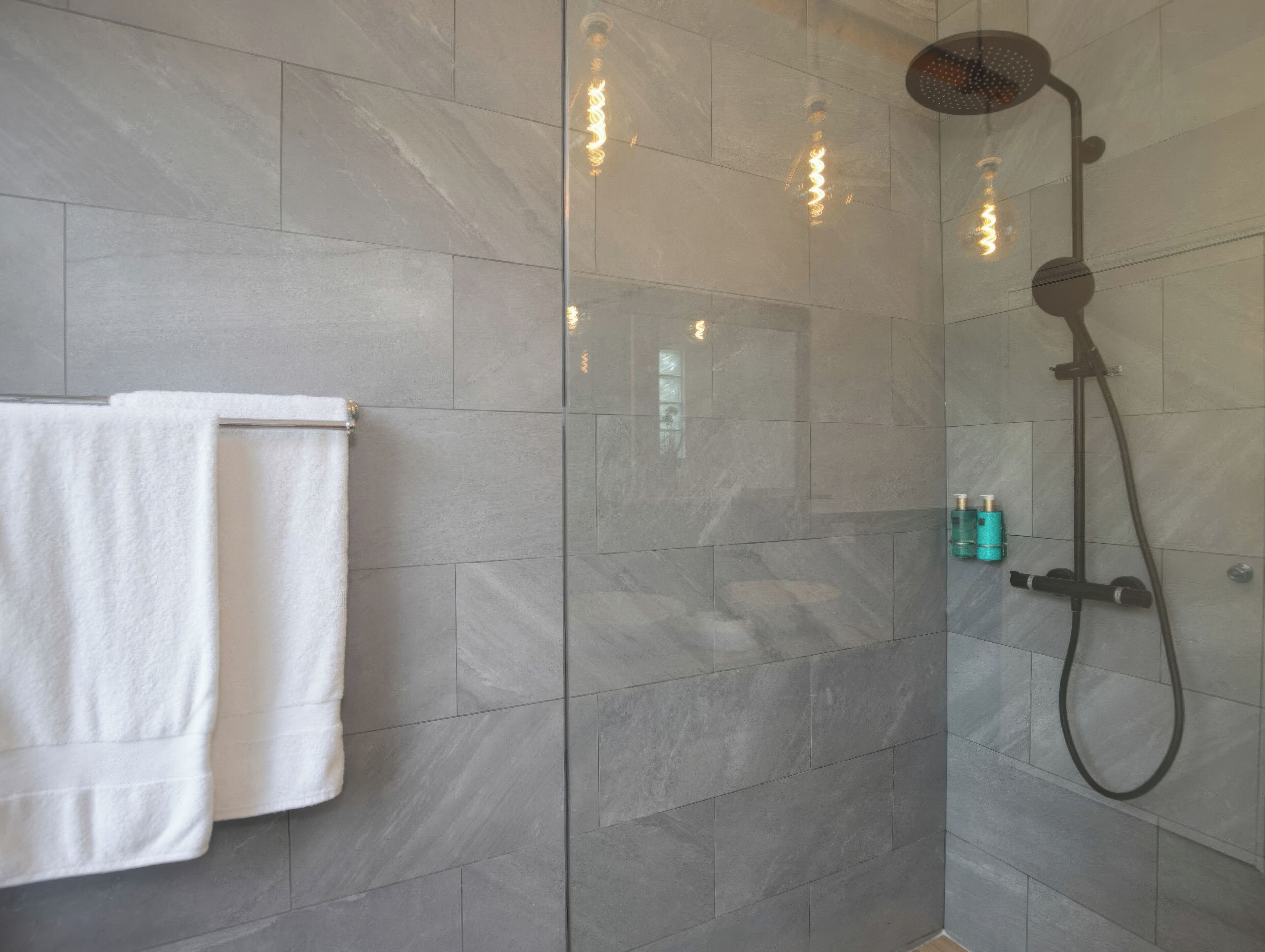 Un baño moderno con ducha de vidrio, una toalla blanca colgada en la pared y dos botellas de champú.