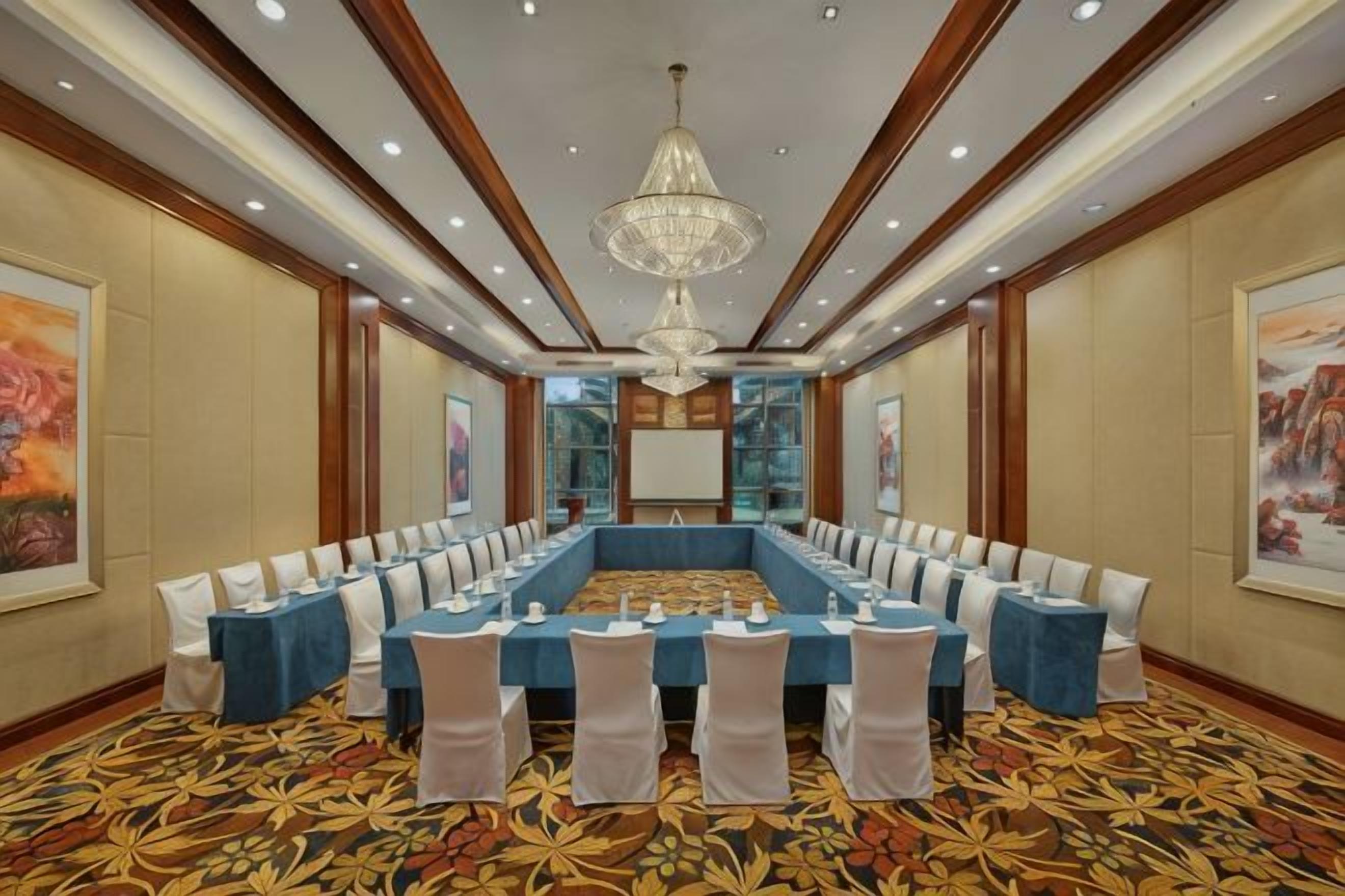 Une salle de conférence avec une longue table, des chaises blanches et un lustre.