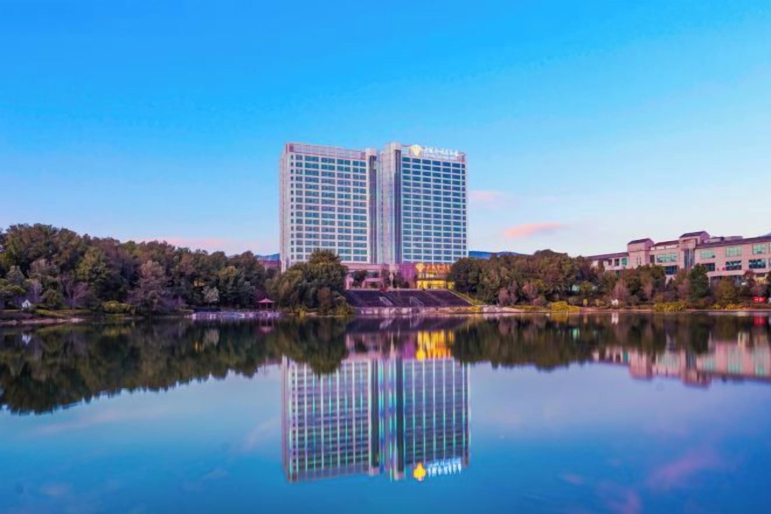 Ein Hochhaus-Hotel mit Spiegelbild in ruhigem Wasser, umgeben von Grünflächen und weiteren Gebäuden.