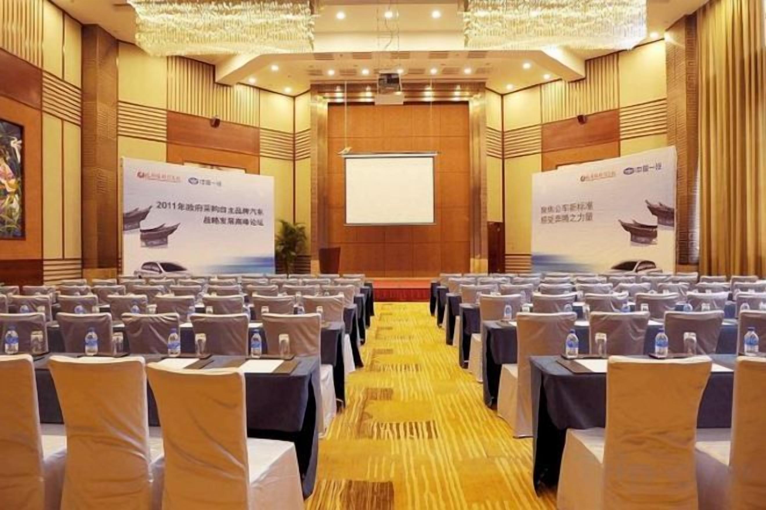 A conference room with rows of tables and chairs, a podium, and a presentation screen.