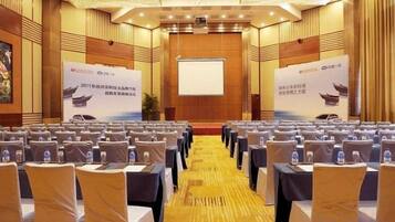 A conference room with rows of tables and chairs, a podium, and a presentation screen.