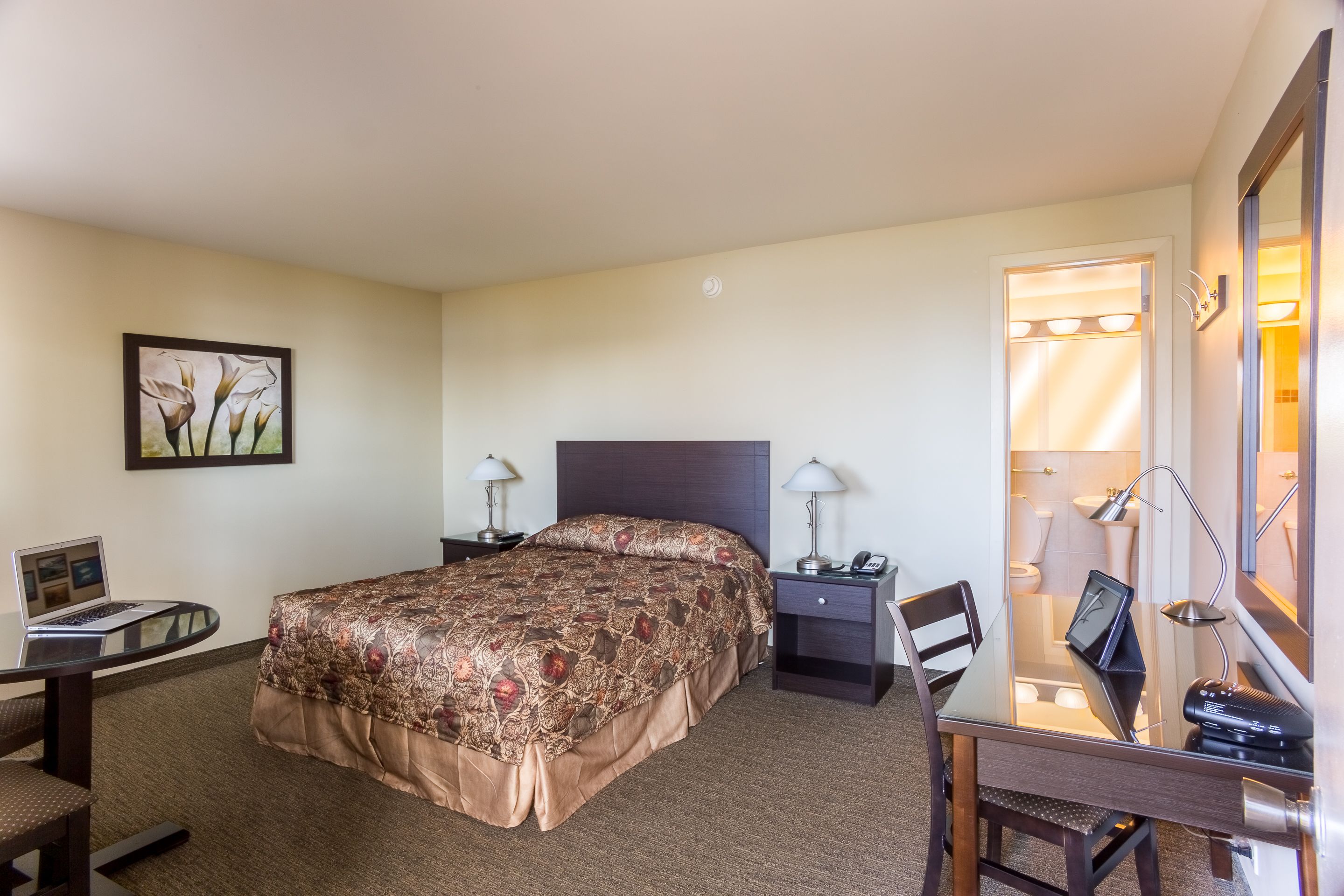 Une chambre d’hôtel comprenant un lit, un bureau avec un ordinateur portable, une chaise, une table de chevet, une lampe et un miroir.