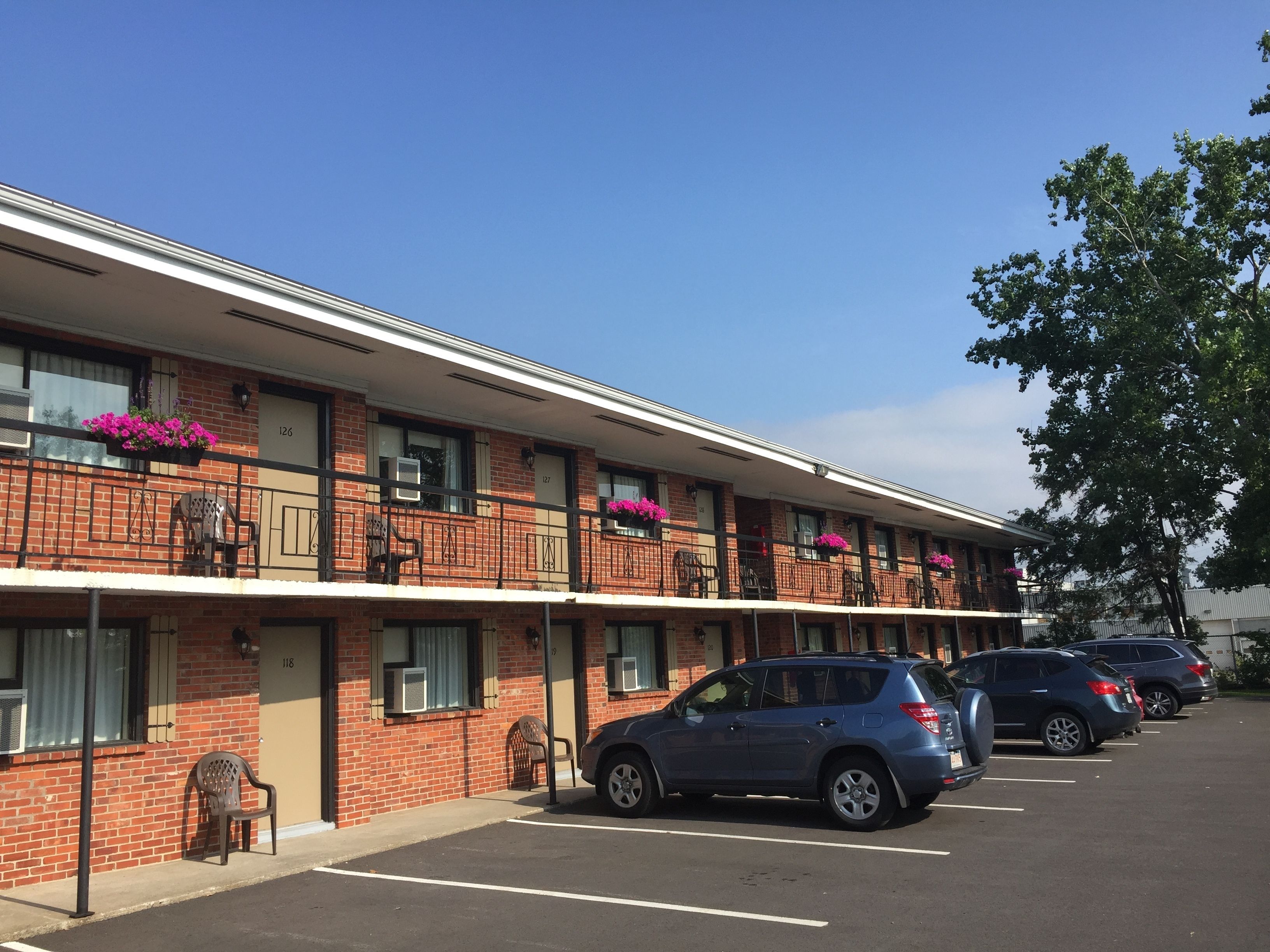 Un motel à étages, avec une façade en briques, des chambres numérotées et un parking où sont garées plusieurs voitures.