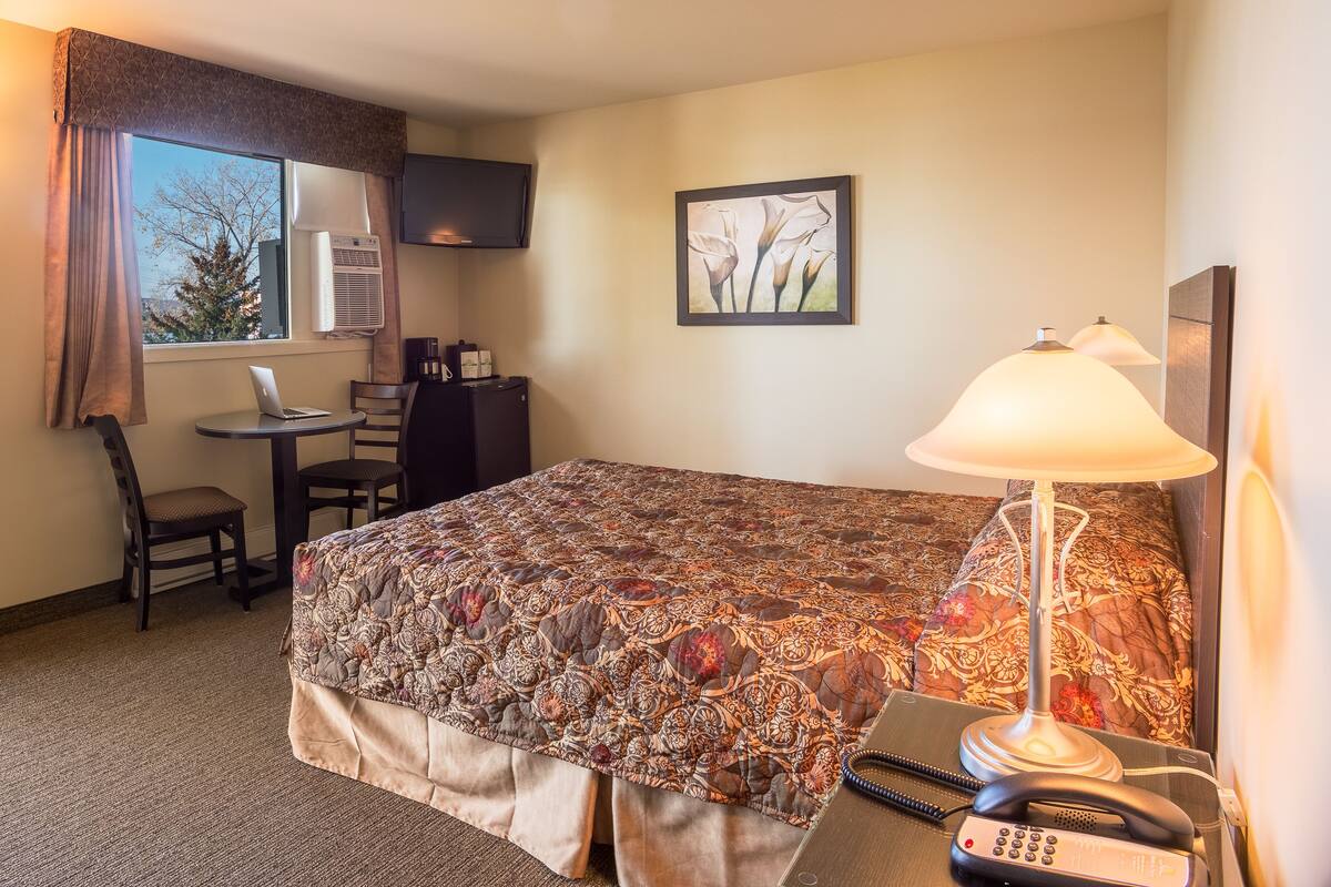 A hotel room with a large bed, a desk with a laptop, a telephone, and a lamp.