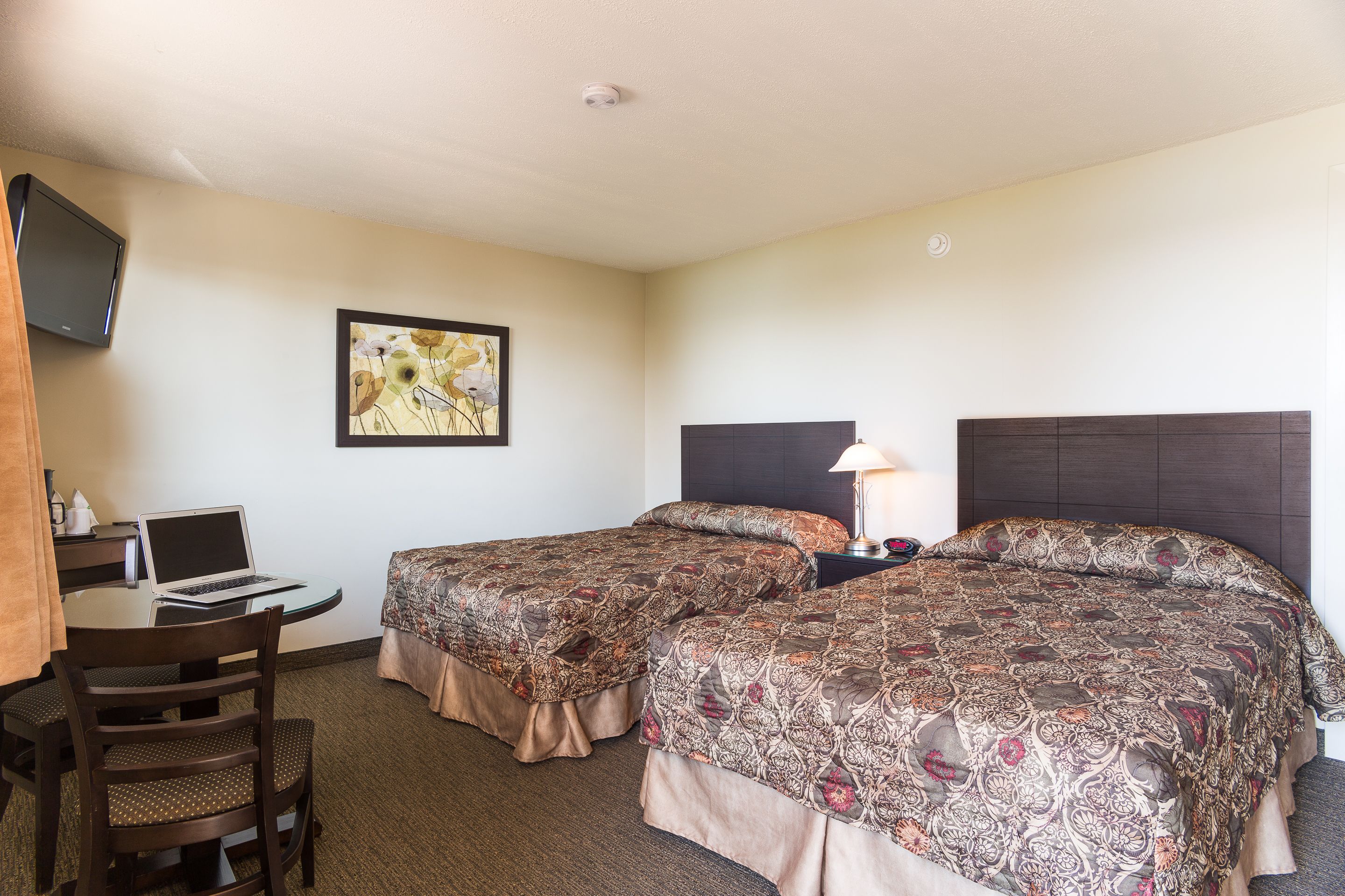 A hotel room with two beds, a desk with a laptop, a television on the wall, and a framed picture.