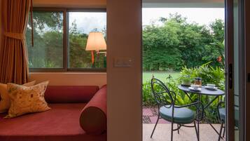 A room with a red sofa, a table with a cup and saucer, and a view of a lush garden through a window.