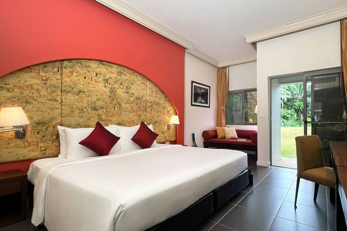 A hotel room with a large bed, a sofa, a desk with a chair, and a view of the outdoors.