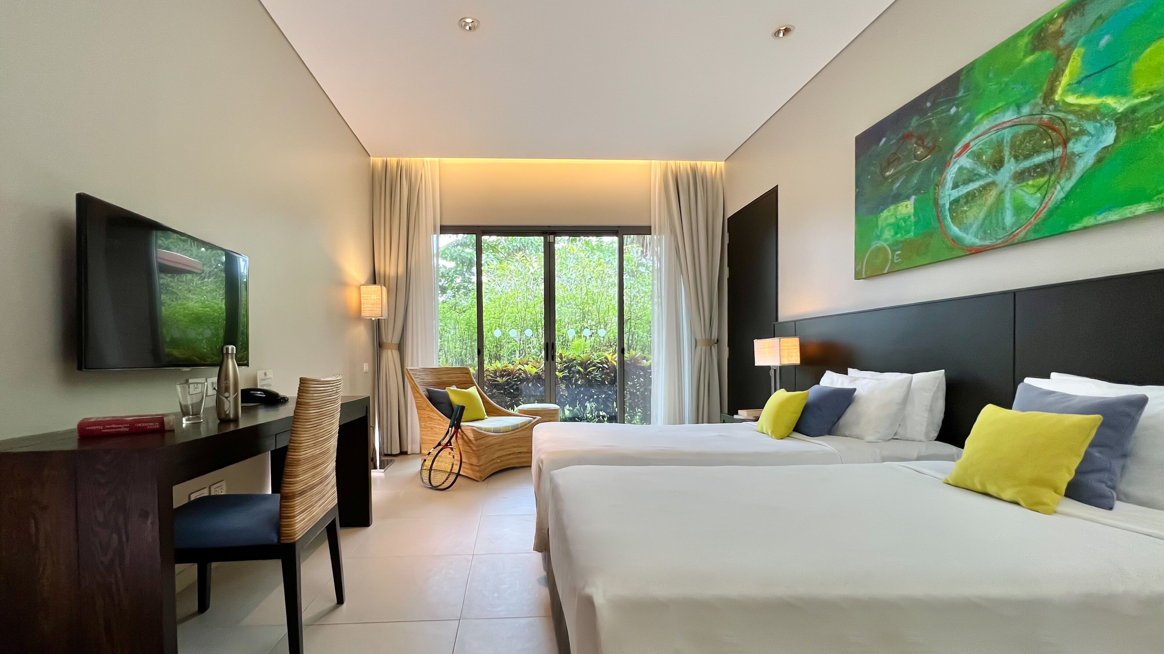 Ein Hotelzimmer mit Bett, Schreibtisch, Stuhl, Fernseher und einem großen Fenster mit Vorhängen.