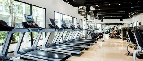 Un gimnasio con numerosas cintas de correr alineadas, amplias ventanas y diverso equipamiento de ejercicio.