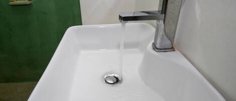 A white sink with running water, a chrome faucet, and a green wall in the background.