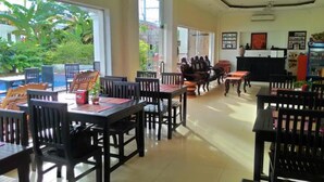 A restaurant with wooden tables and chairs, large windows, and a view of greenery outside. - King Boutique Hotel (Siem Reap)