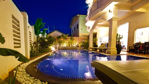 A swimming pool with a tiled edge, surrounded by pebbles and plants, with a building in the background. - King Boutique Hotel (Siem Reap)