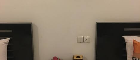 A hotel room with two beds, a small table with a remote control, a red object, and a wooden box.
