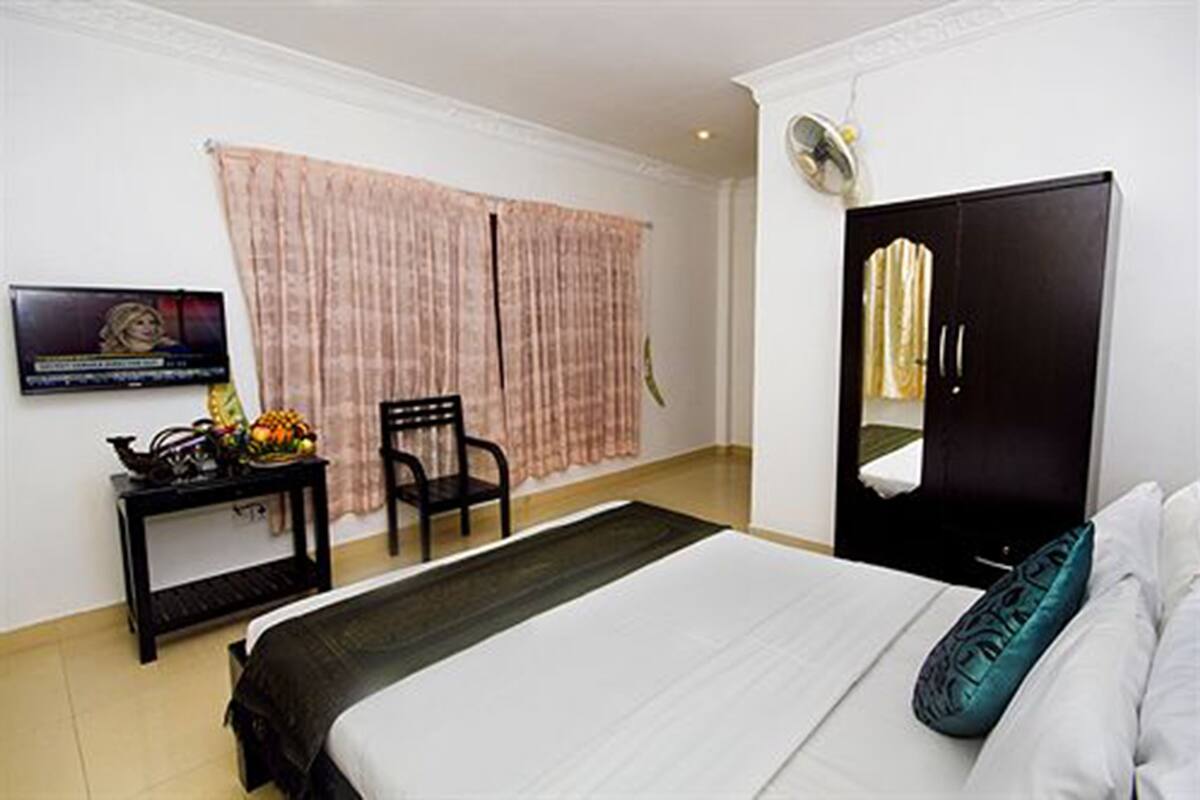 Habitación de hotel con cama, una silla, una mesita con frutero, televisión y armario.