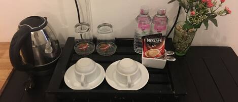 Una estación de café con cafetera, dos tazas, un sobre de Nescafé y un florero con flores.