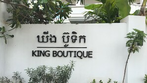 A white wall with the text "KING BOUTIQUE" in both English and another script, surrounded by various plants and greenery. - King Boutique Hotel (Siem Reap)