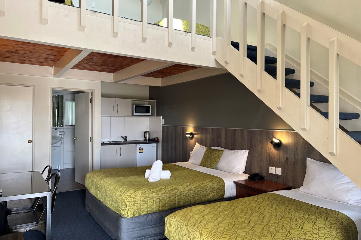 A hotel room with two beds, a kitchenette, and a staircase.