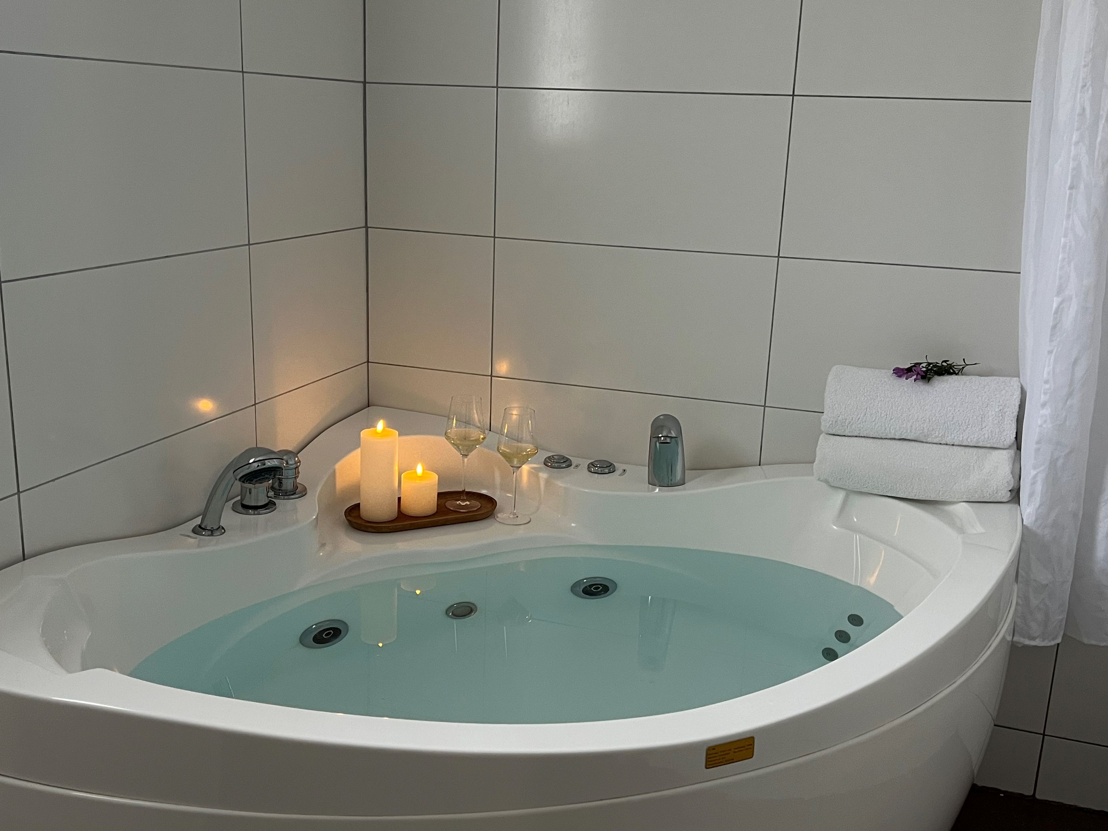 Een bubbelbad in een spa met kaarsen, een glas water en een handdoek.