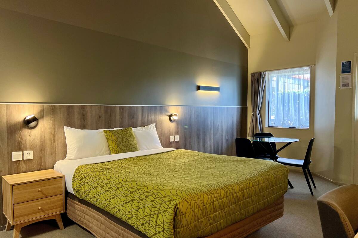 A hotel room with a large bed, bedside tables, a desk, and a window with curtains.