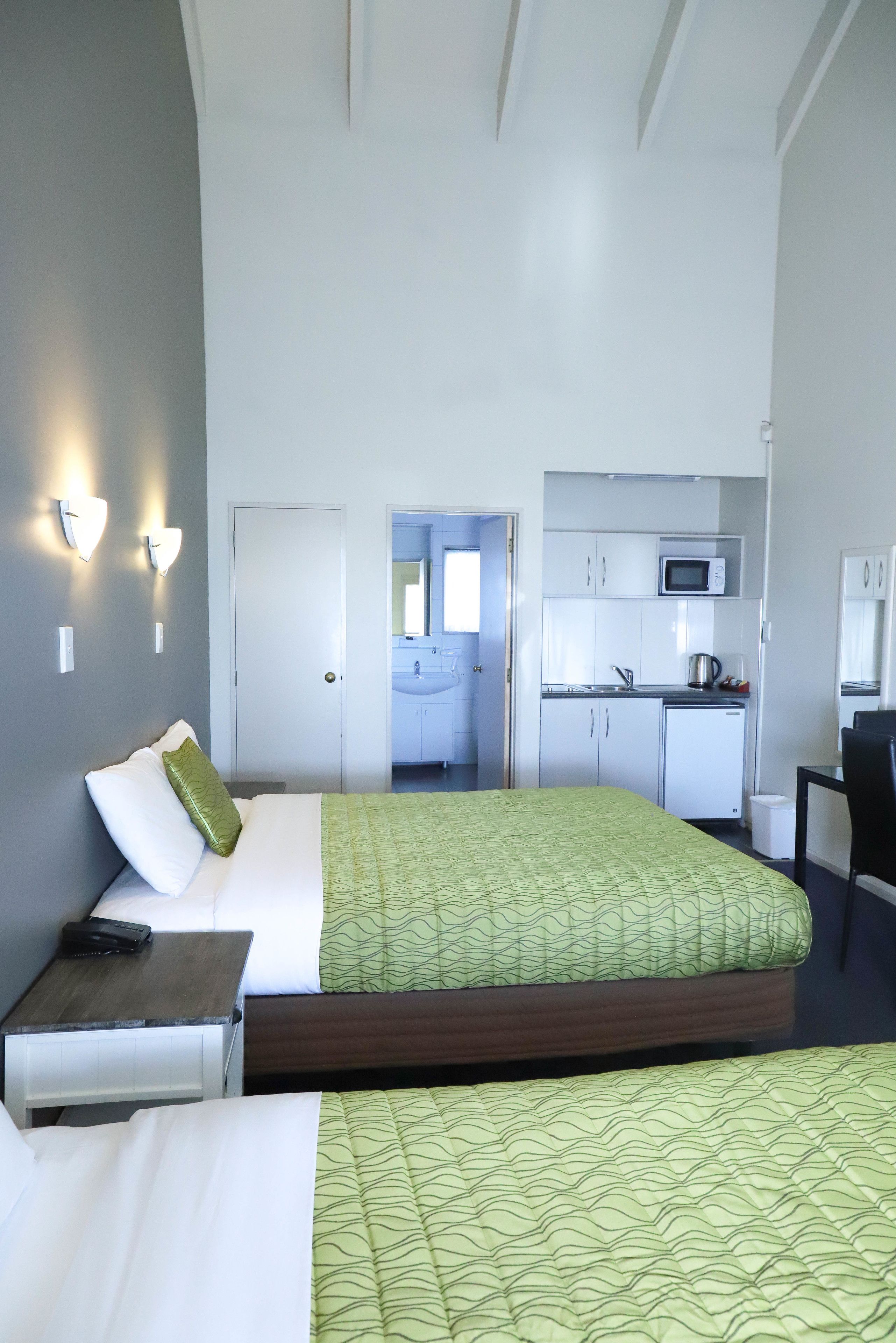 A hotel room with a bed, bedside table, and a view into a kitchenette area.