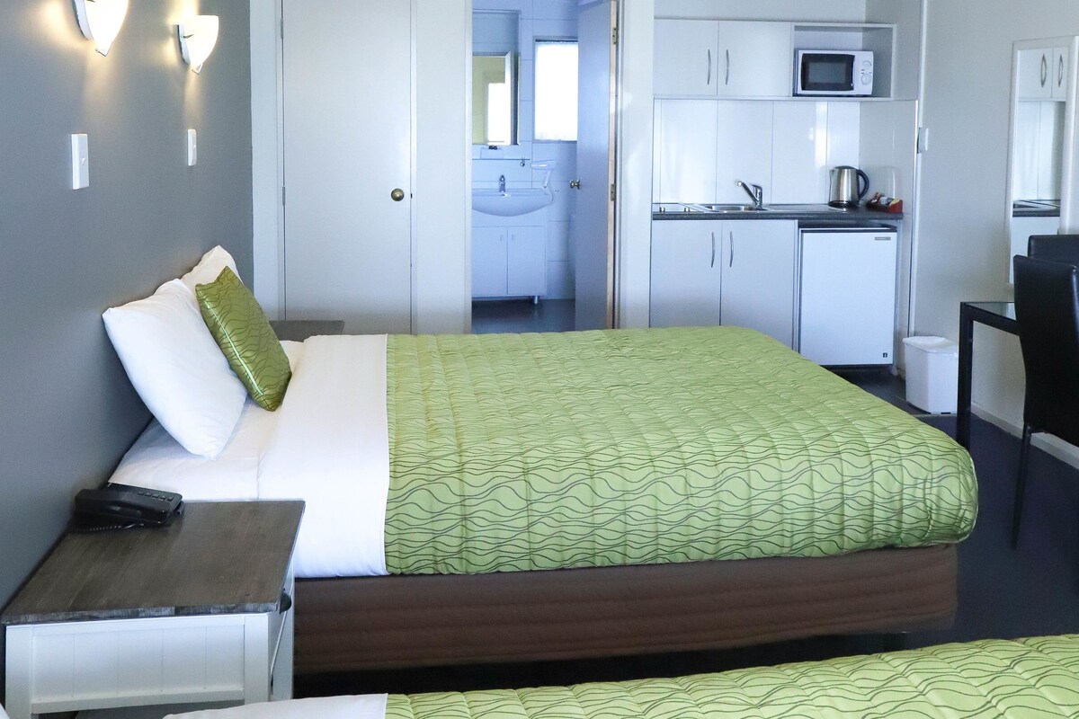 A hotel room with a bed, bedside table, and a view into a kitchenette area.