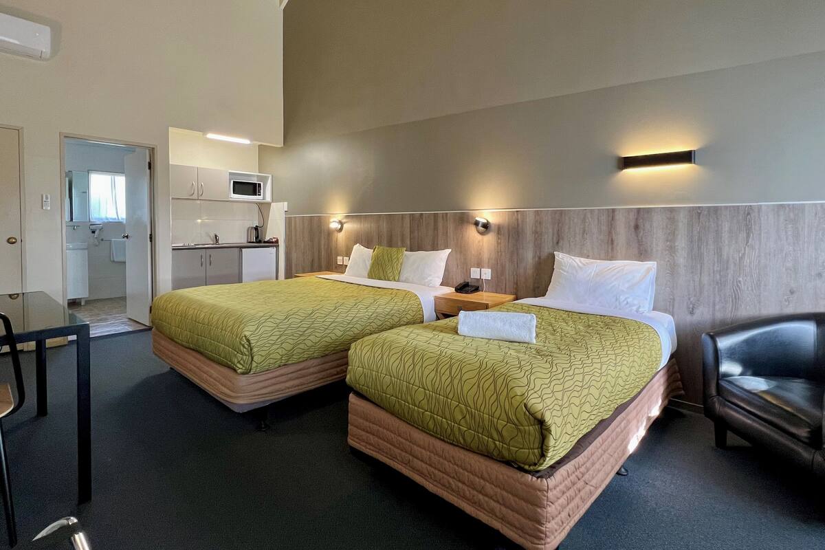 A hotel room with two beds, a desk, a chair, a microwave, and a small kitchenette.