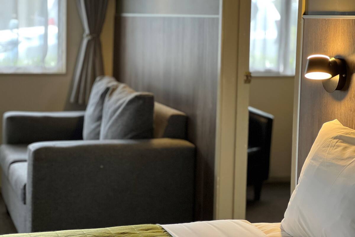 A hotel room with a bed, a grey sofa, and a wall-mounted light fixture.