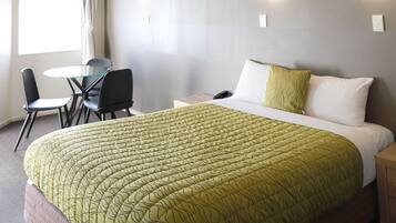 A hotel room with a bed, a desk, two chairs, and a window with curtains.