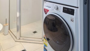 A front-loading LG washer and dryer unit with a glass shower enclosure adjacent to it. - Apartments on Chapman (North Melbourne)
