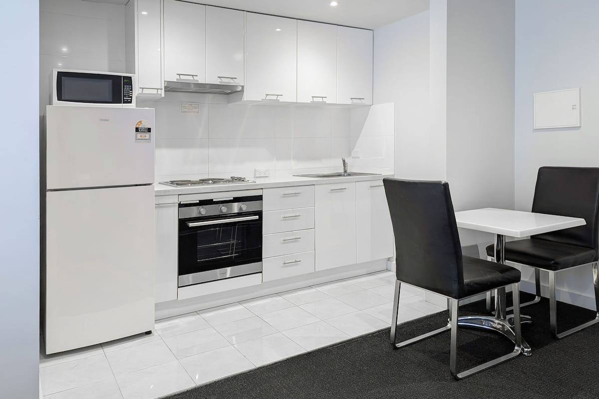 Eine moderne Küche mit weißen Schränken, einem eingebauten Backofen, einer Mikrowelle und einem Essbereich mit Tisch und Stühlen.