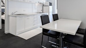 A modern kitchen with white cabinetry, a built-in microwave, and a dining area with a white table and black chairs. - Apartments on Chapman (North Melbourne)