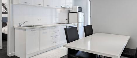 Una cocina moderna con armarios blancos, microondas integrado y un comedor con mesa blanca y sillas negras.