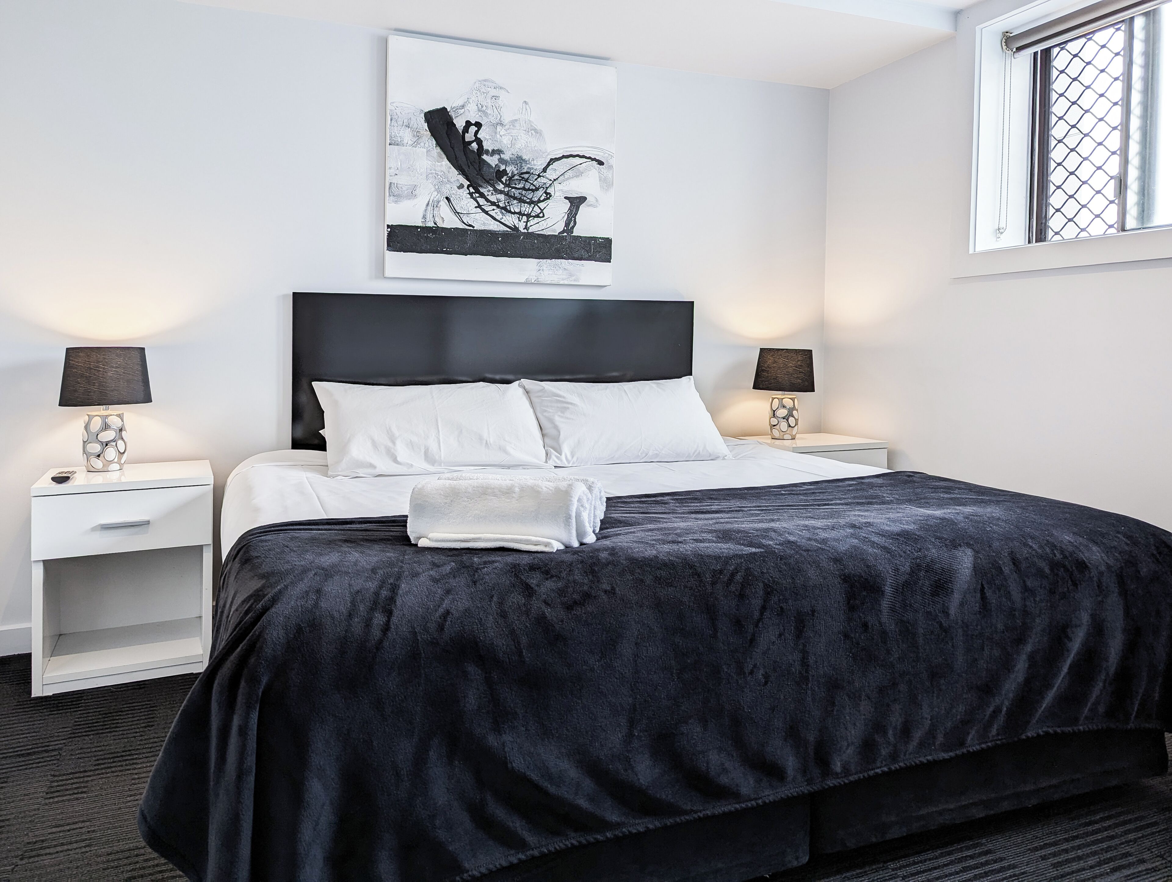 A modern hotel room with a large bed, two bedside tables, a headboard, and a window with a view.