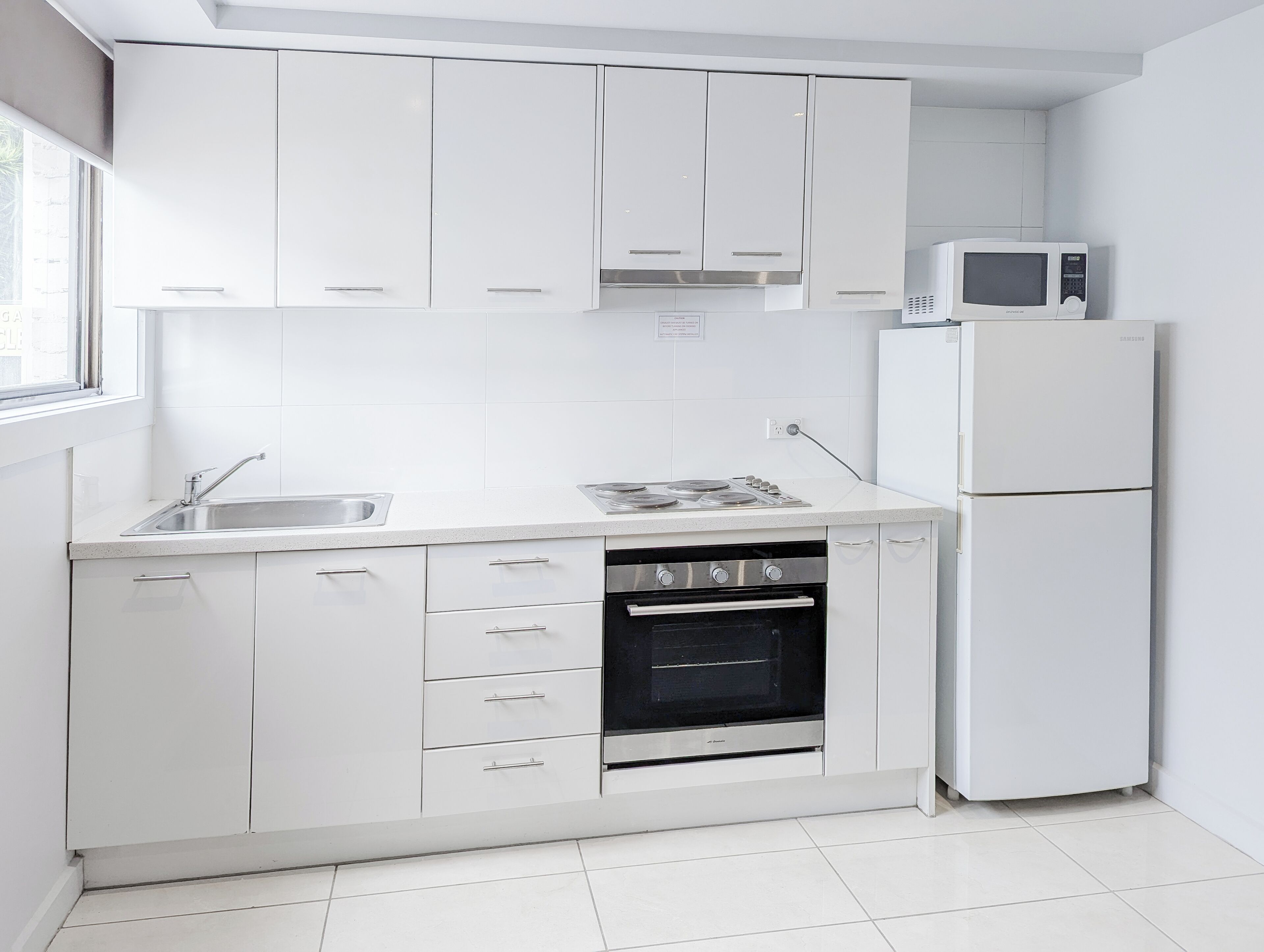 A modern kitchen with white cabinetry, a stainless steel sink, a built-in microwave, a refrigerator, and a stove.