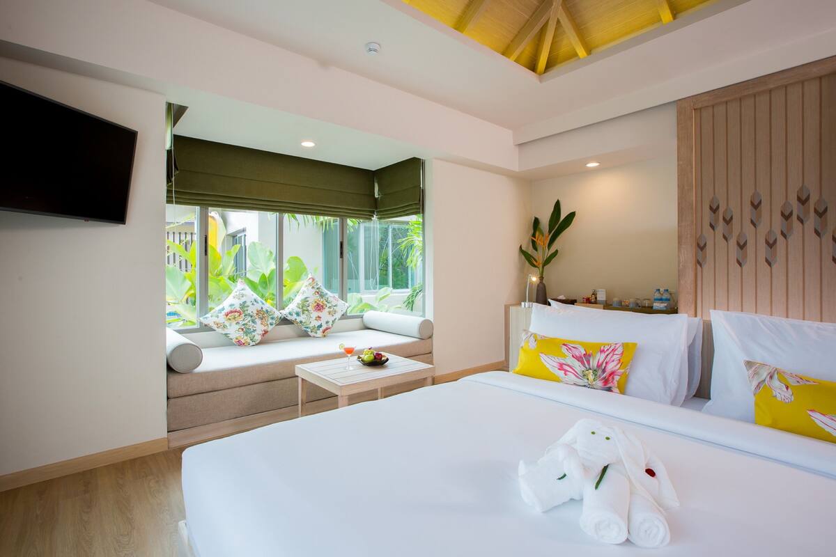 A modern hotel room with a large bed, a sofa with a view, a flat-screen TV, and a small table with a drink.