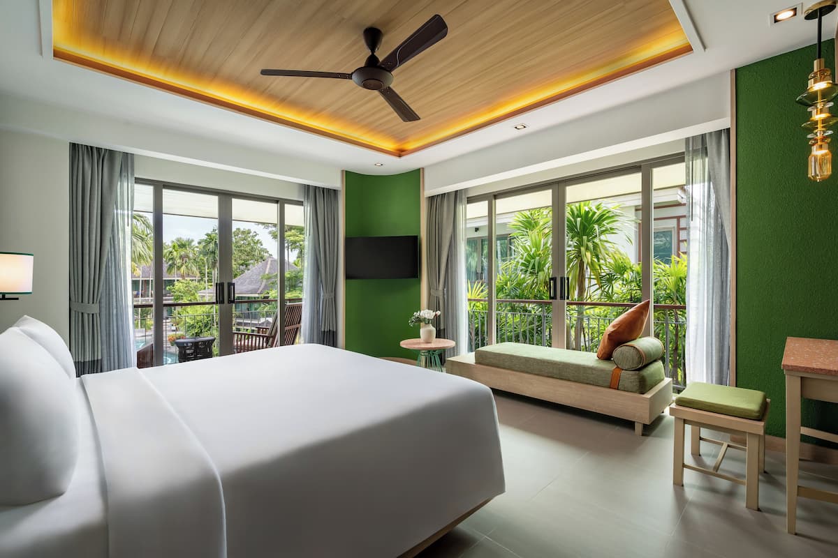 A modern hotel room with a large bed, a ceiling fan, a sofa, a small table, and a TV.