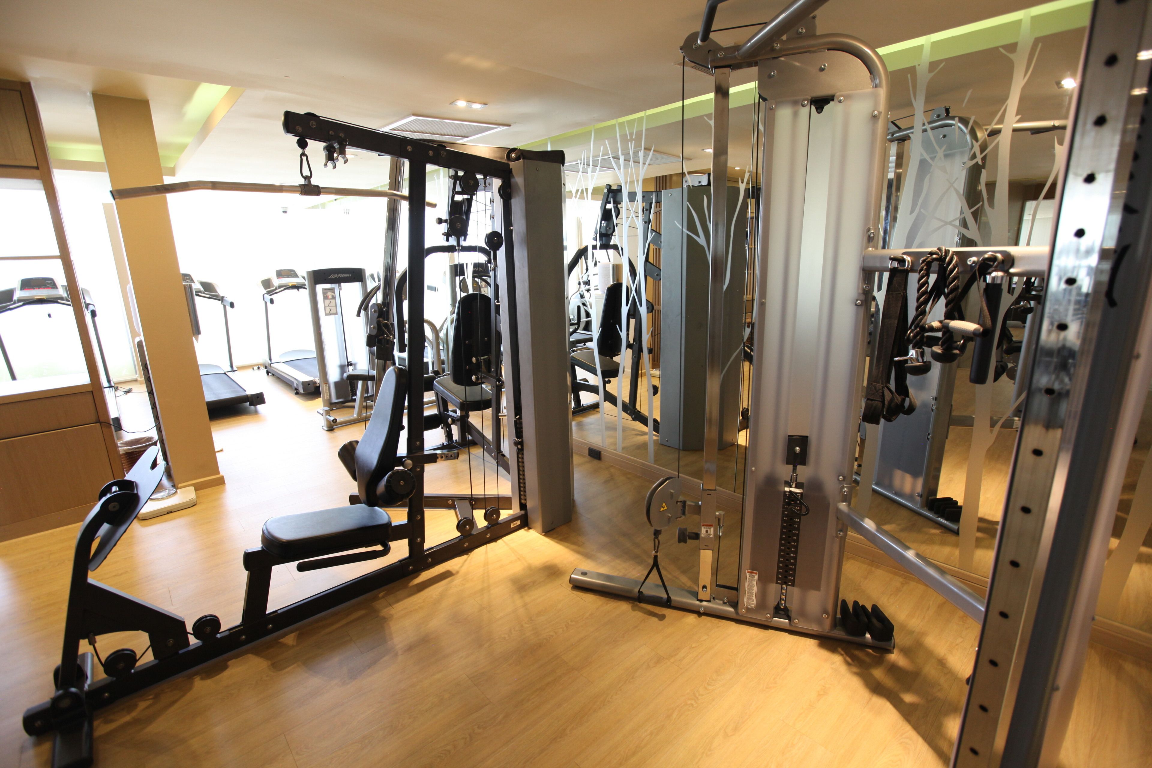 Ein Fitnessstudio mit verschiedenen Trainingsgeräten, Holzboden und Spiegeln.