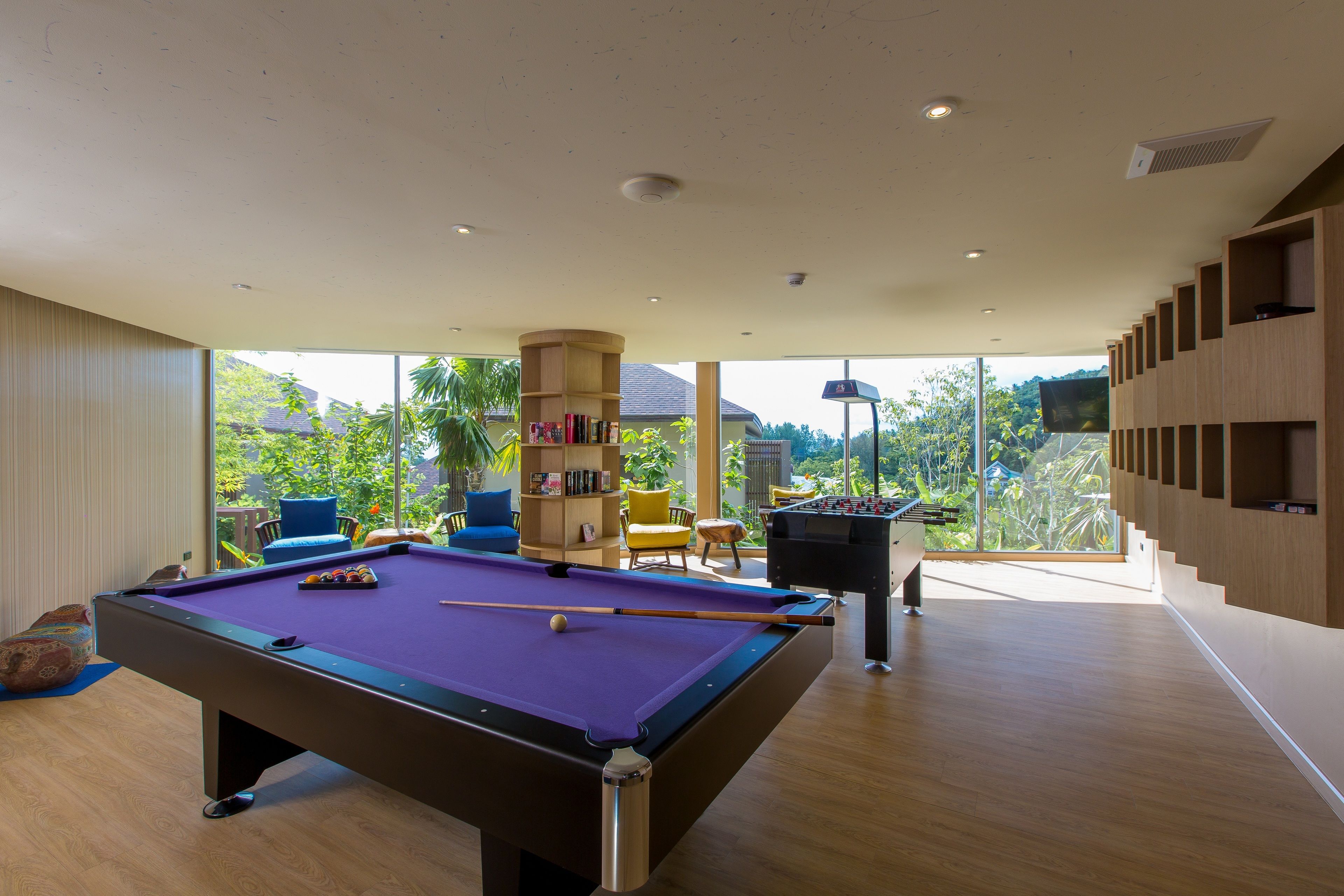A pool table in a room with a view of greenery outside.