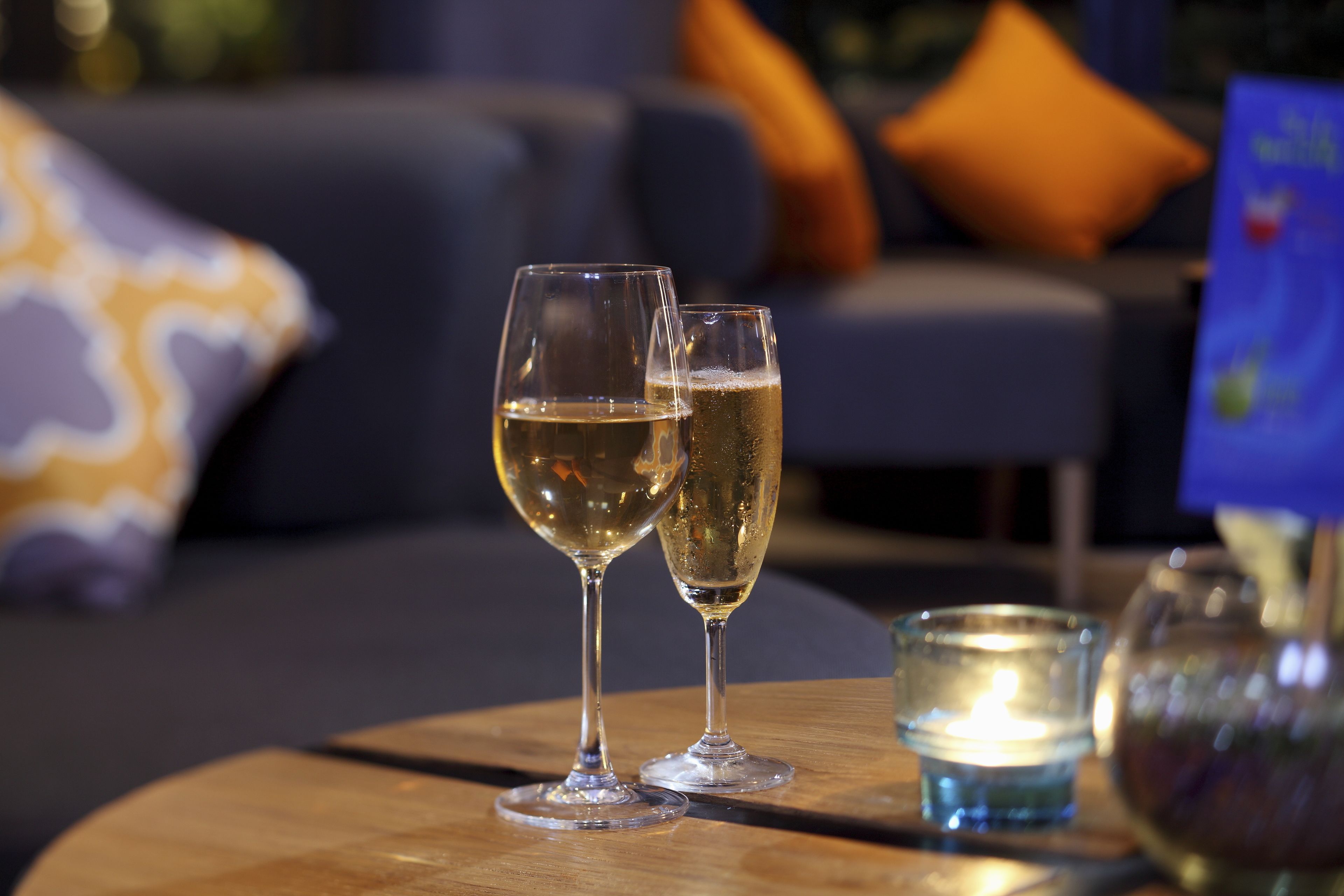 Two glasses of champagne on a wooden table with a lit candle and a vase.