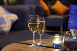 Two glasses of champagne on a wooden table with a lit candle and a vase.