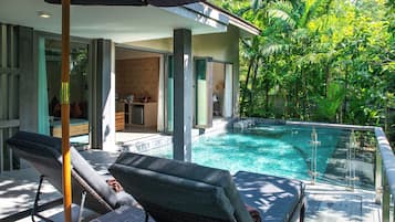 A poolside area with lounge chairs, a glass-enclosed kitchen, and lush greenery.