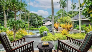 Un entorno de resort tropical con piscina, abundante vegetación y dos sillas de madera con cojines.