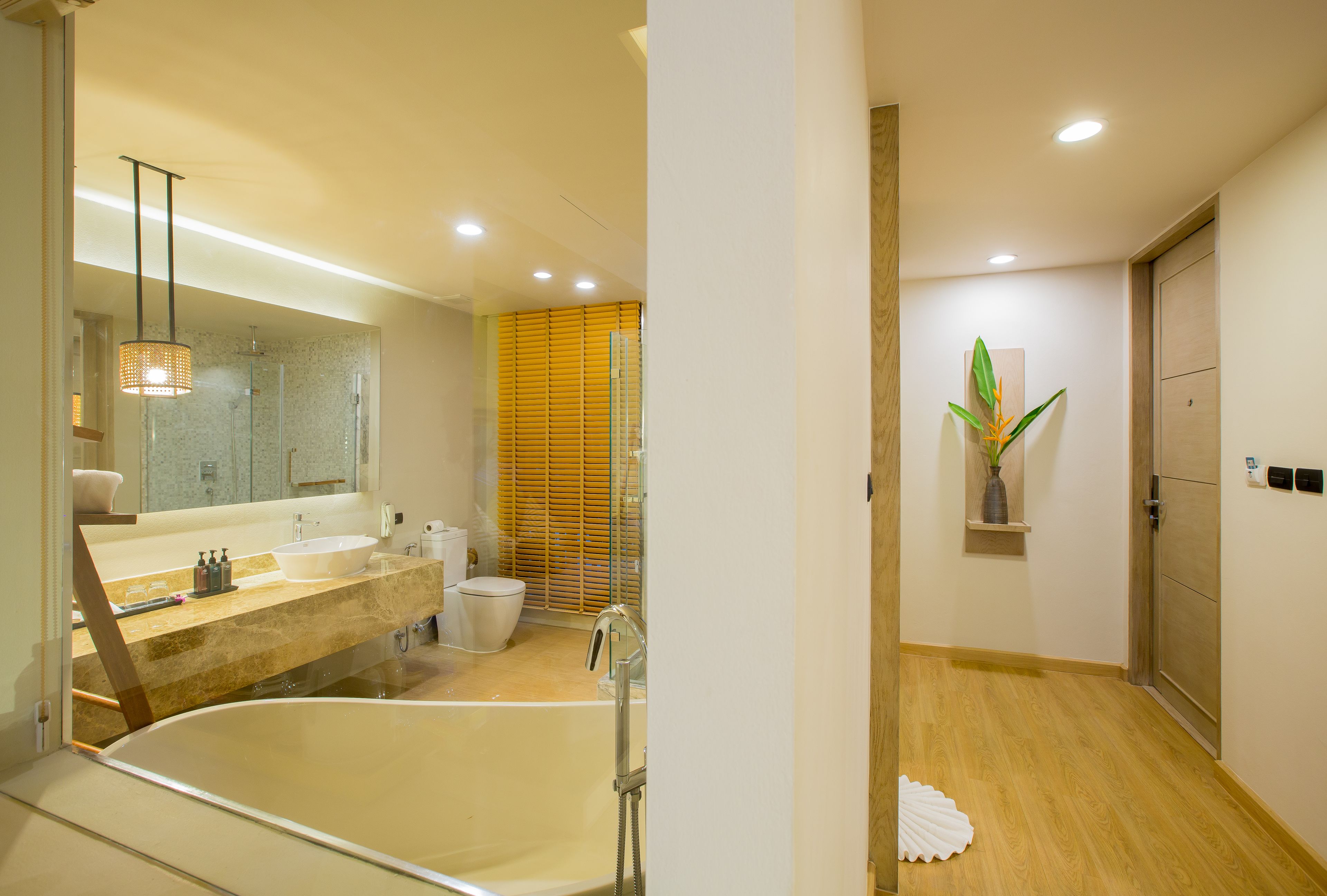 Une salle de bain moderne avec une grande baignoire, un lavabo et des toilettes. Un miroir est placé au-dessus du lavabo et une plante décore le mur.
