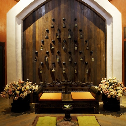 A room with a large wooden wall, a bench with cushions, and two flower arrangements.