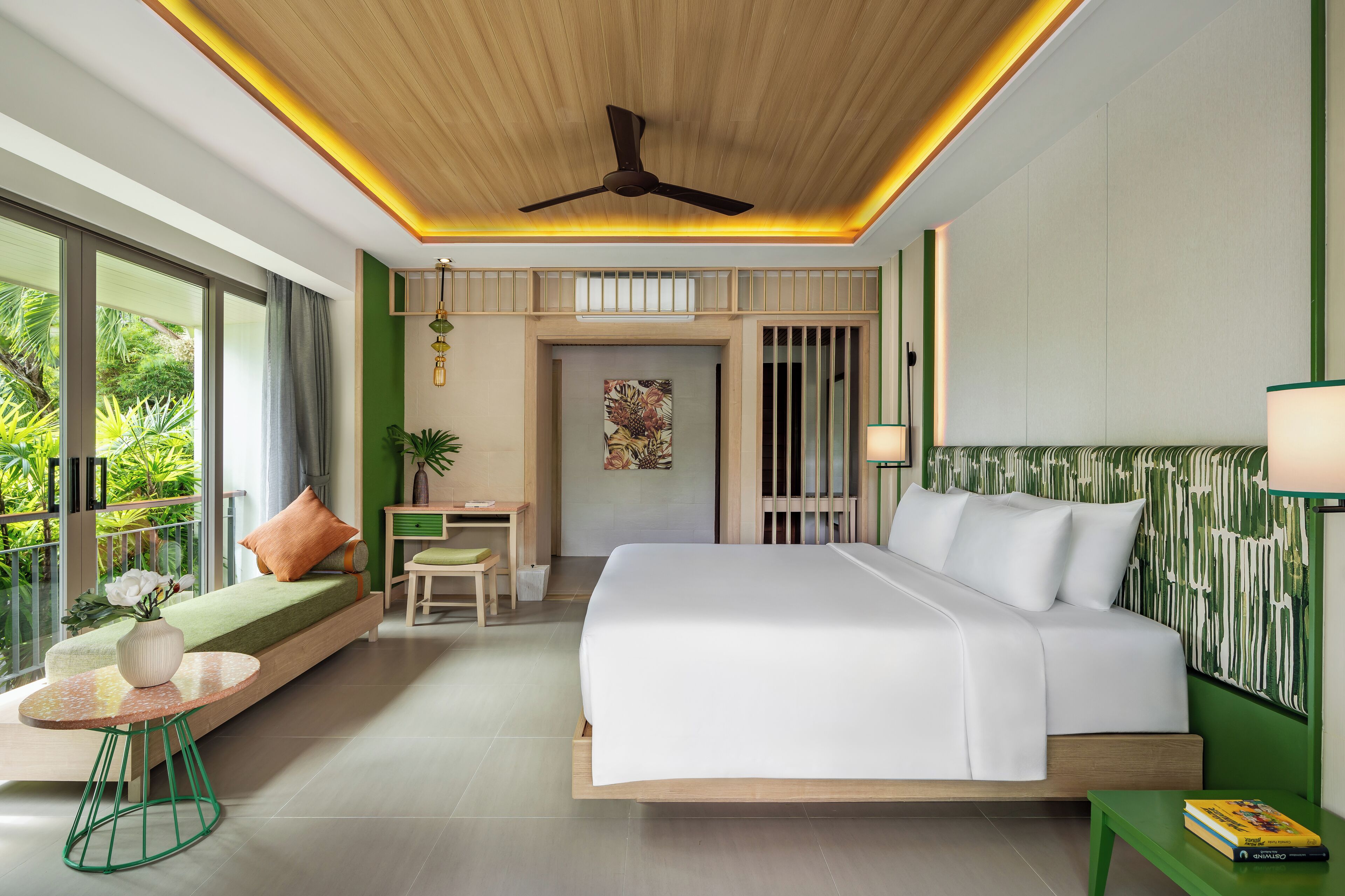 A modern bedroom with a large bed, a seating area, a desk, and a view of greenery.