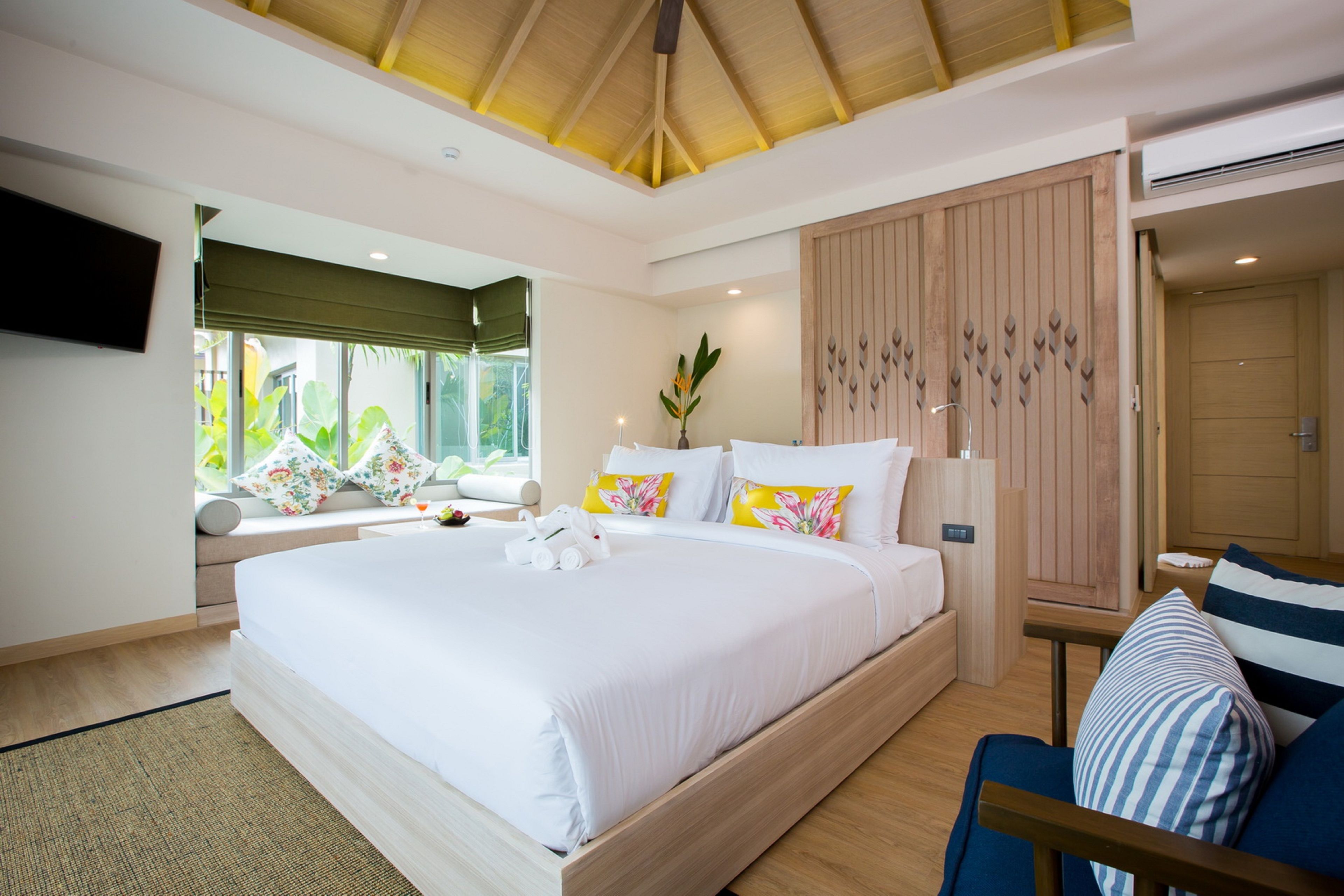 A modern bedroom with a large bed, a wooden headboard, a bedside table, and a TV mounted on the wall.