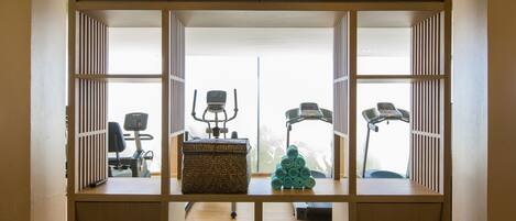 A room with a treadmill, exercise equipment, a wicker basket, and a small Christmas tree.