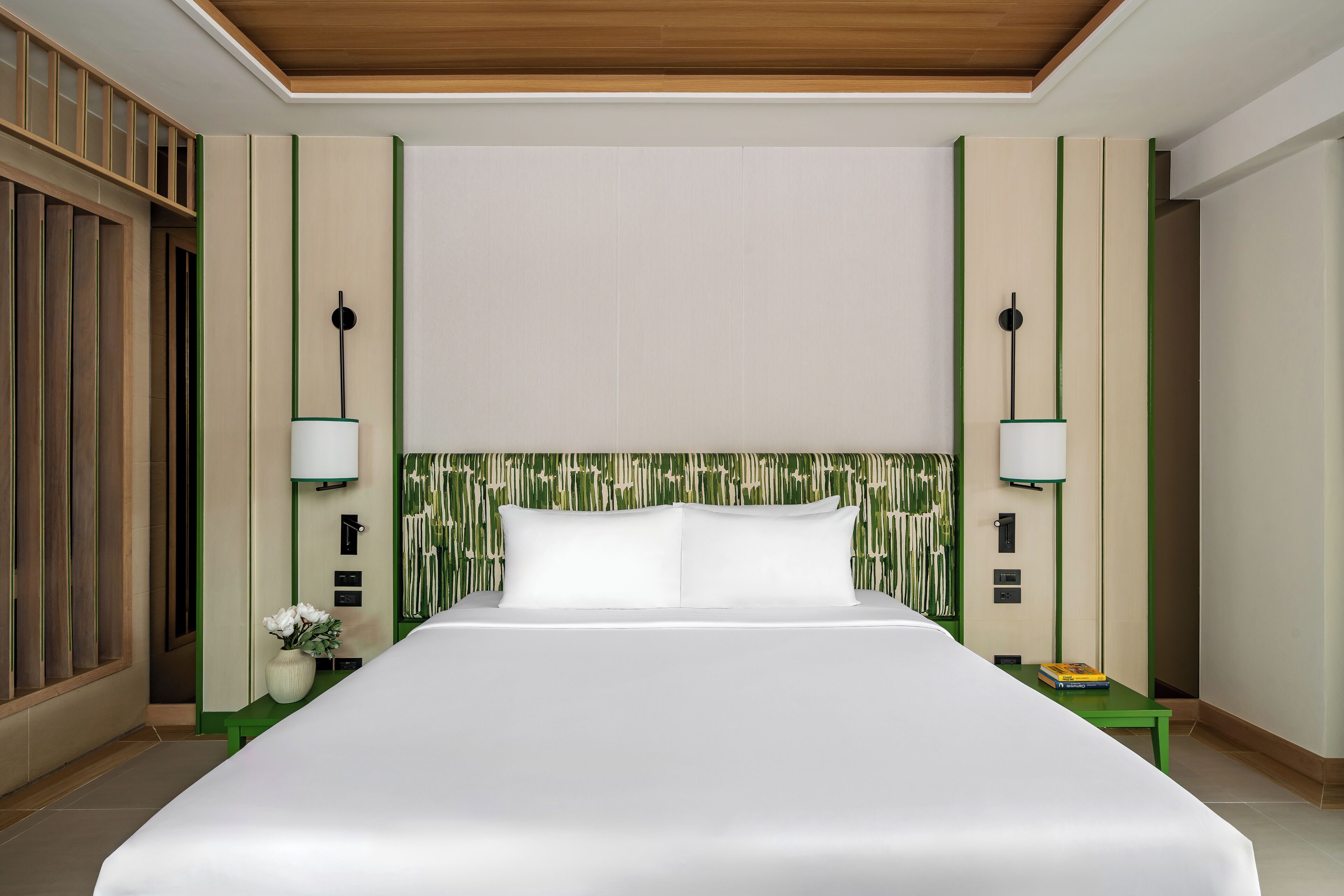 A hotel room with a large bed, two bedside tables, a green accent wall, and a wooden ceiling.